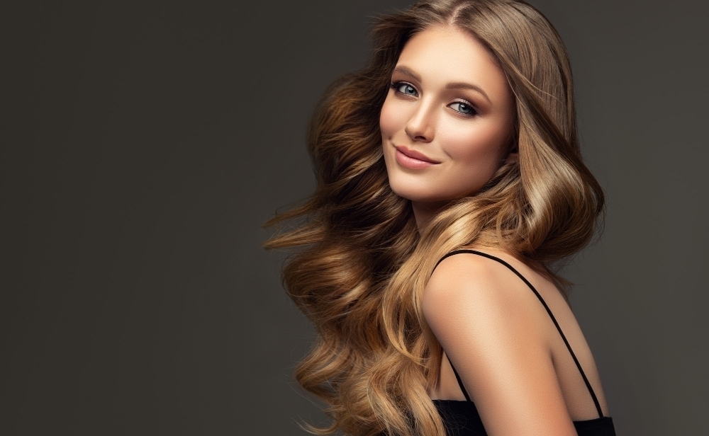 Perfect well groomed curly long deep blonde hair is surrounding pretty smiling face of young woman