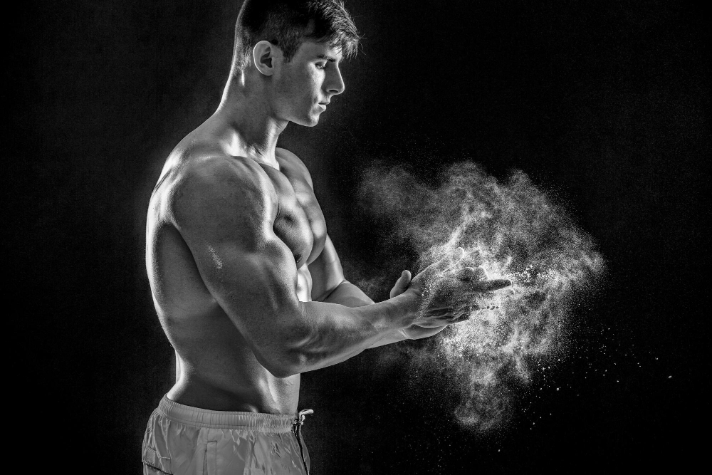 Young muscular man preparing to hand lifting heavy weight. White talcum dynamically scatters in different directions. Black and white. stands sideways