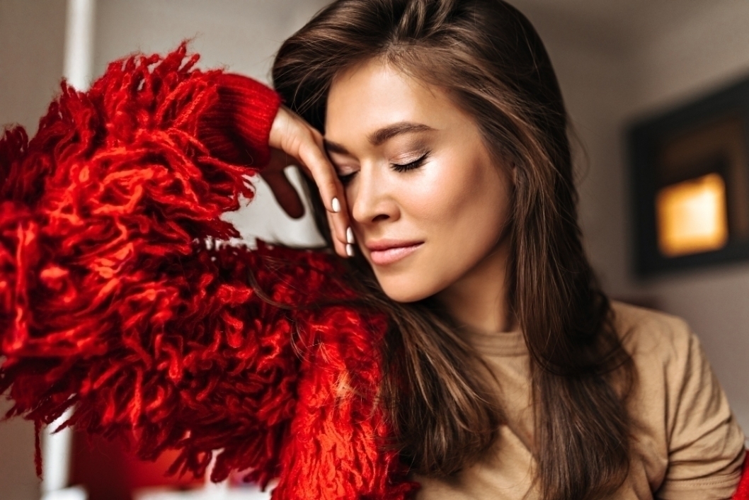 Tanned dark haired woman in beige T shirt leaned against wall. Portrait of attractive lady wearing red jacket.